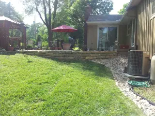 Low limestone ledge wall along a sloped side yard with a river rock swale beside the home